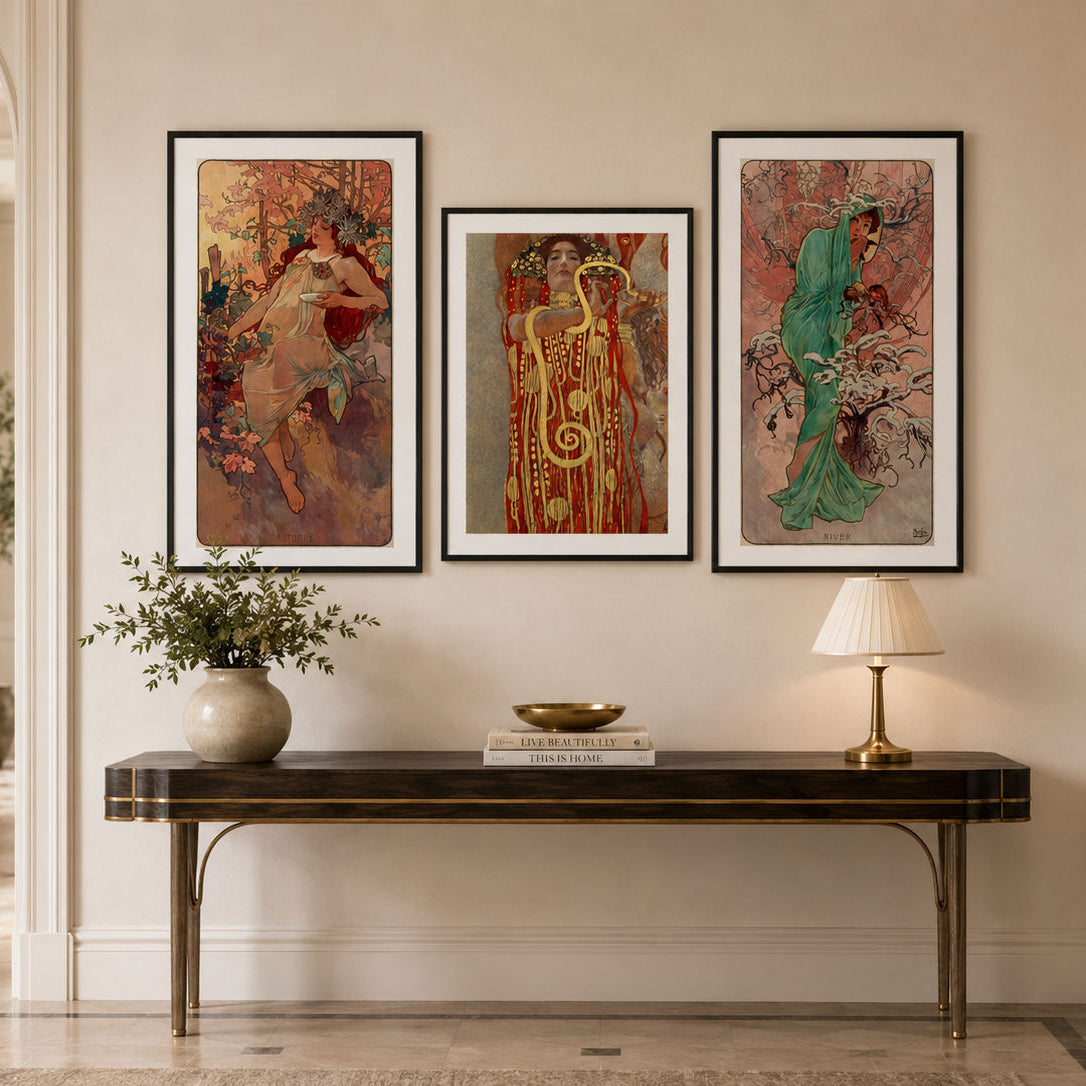 Three framed art prints featuring classical figures in warm and vibrant tones, displayed on a beige wall above a dark console table in a beautifully styled interior hallway.