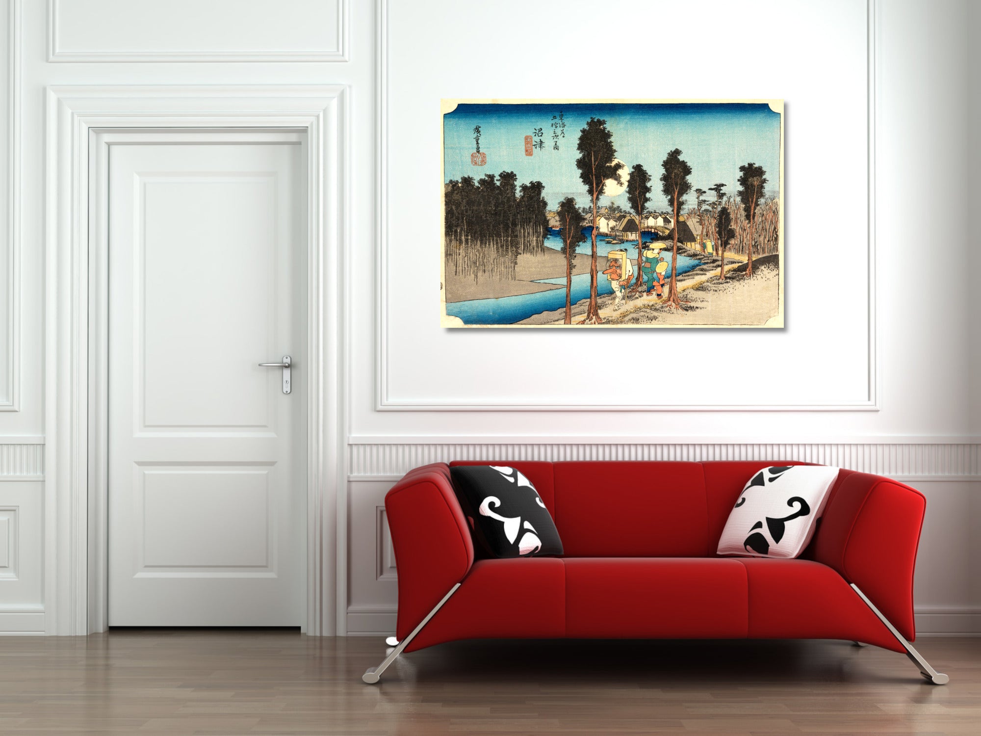 A framed Japanese-style landscape art print hangs on a white wall above a modern red sofa with black-and-white patterned pillows in a bright room.