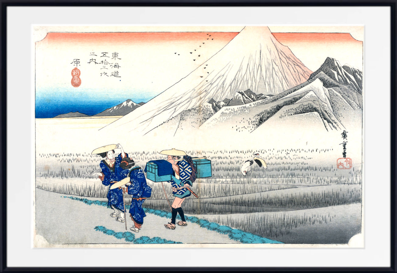 A framed Japanese-style art print depicting Mount Fuji with workers in blue garments walking through a field in the foreground, shown against a white mat and black frame.