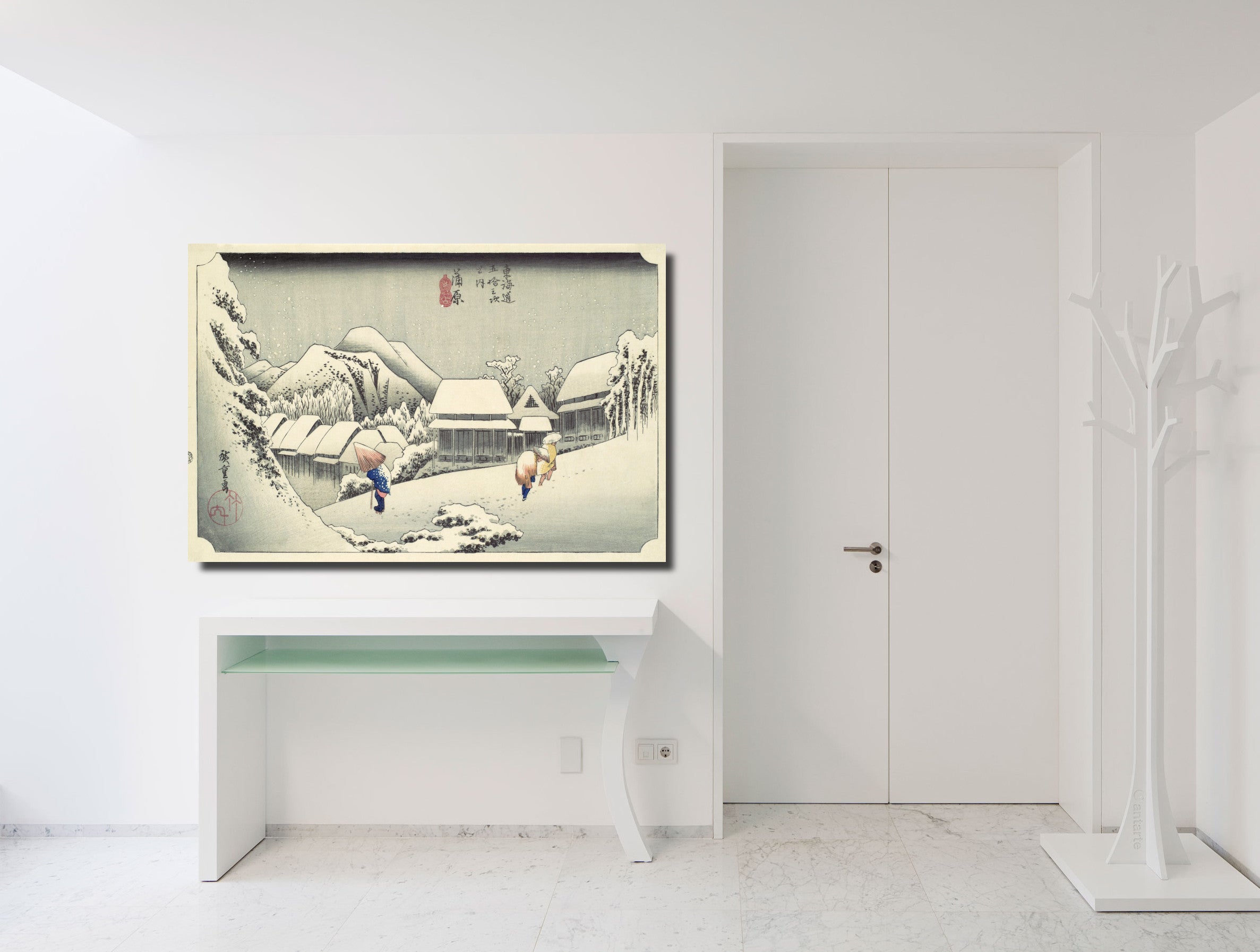 A framed Japanese-style winter landscape art print hangs on a white wall above a white console table in a bright, modern minimalist room.