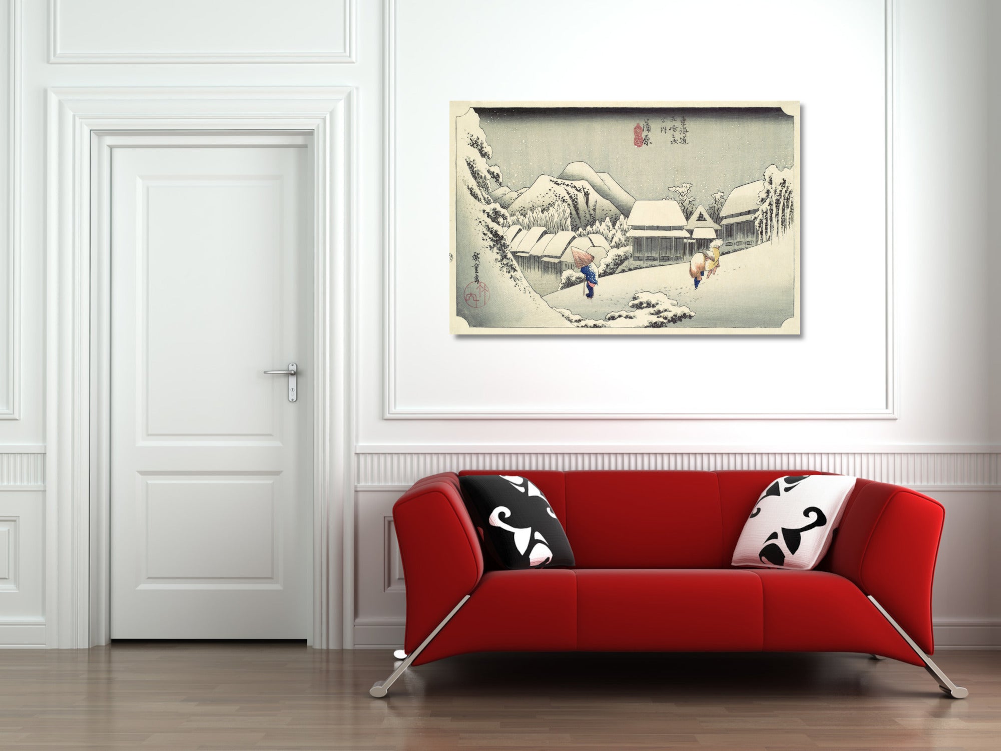 A framed Japanese-style winter landscape print hangs on a white paneled wall above a bright red sofa with black-and-white patterned pillows in a modern living room setting.