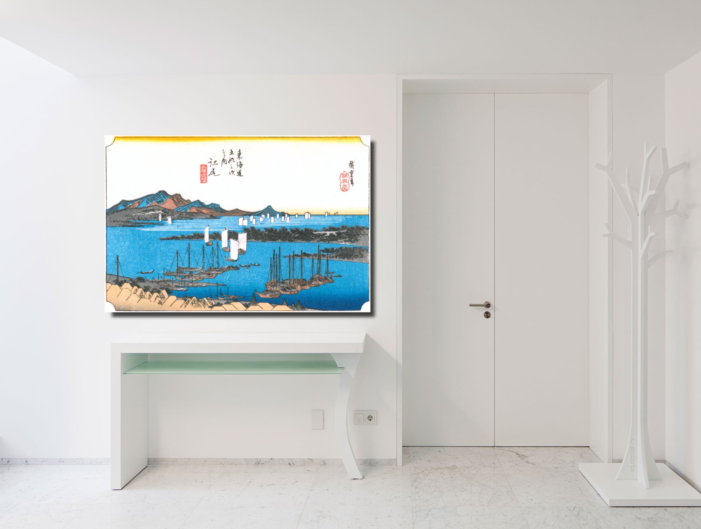 A framed Japanese ukiyo-e style art print depicting a harbor scene with blue water, boats, and mountains, displayed on a white console table in a minimalist white room.