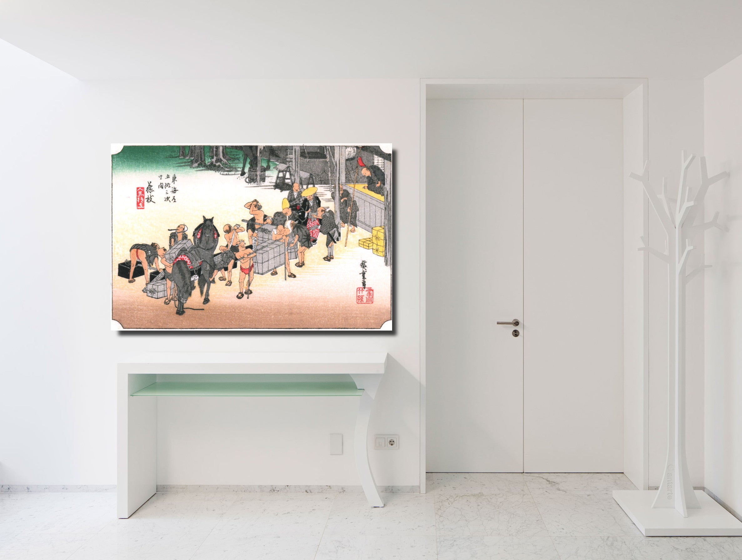 A framed art print depicting a traditional Japanese street scene with figures and horses, displayed on a white wall above a console table in a minimalist white room.