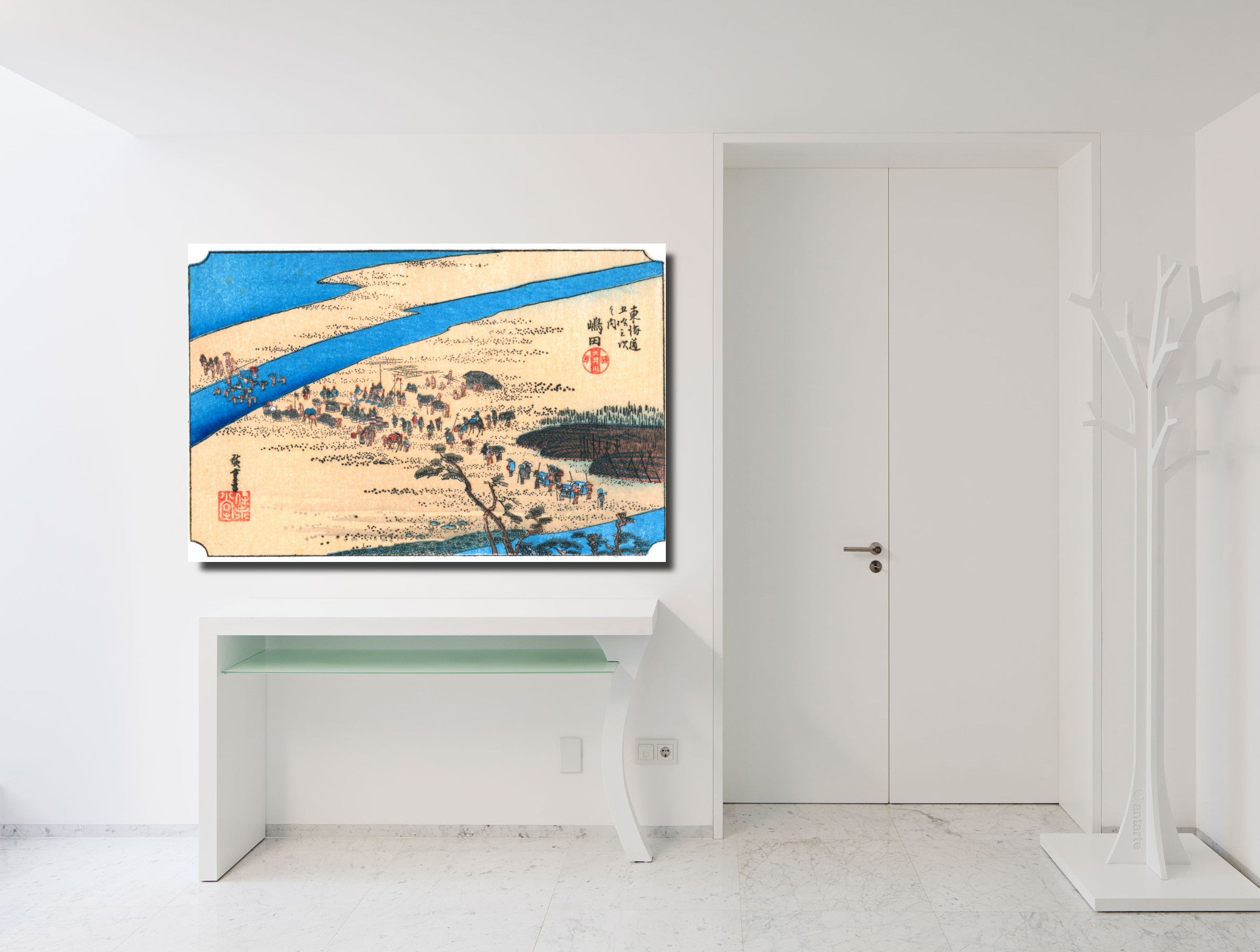 A framed Japanese ukiyo-e woodblock print depicting a river landscape with figures and boats, displayed on a white wall above a white console table in a minimalist room.