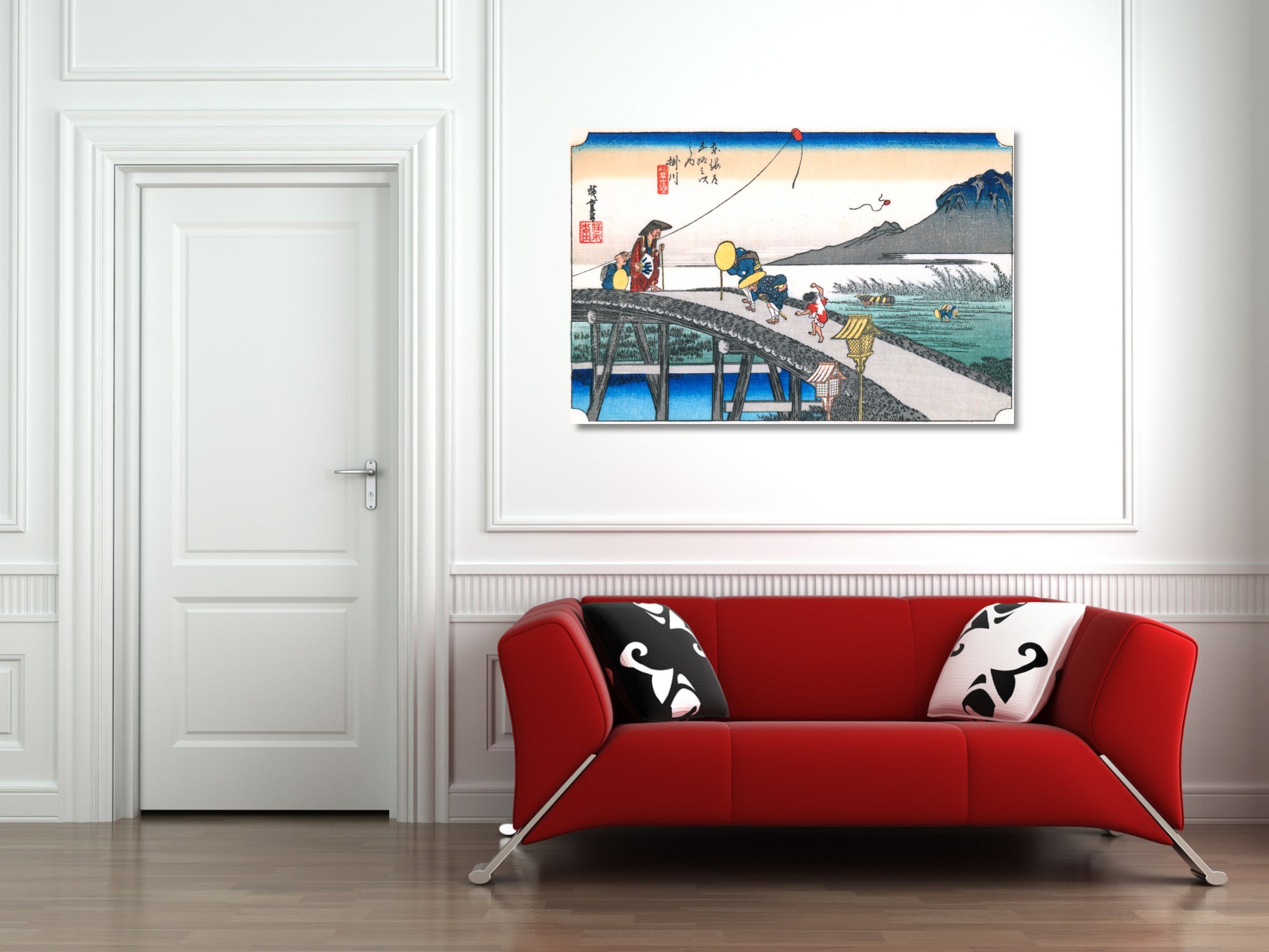A framed Japanese-style art print depicting a fishing scene on a pier, displayed on a white wall above a modern red sofa with black and white patterned pillows in a living room setting.