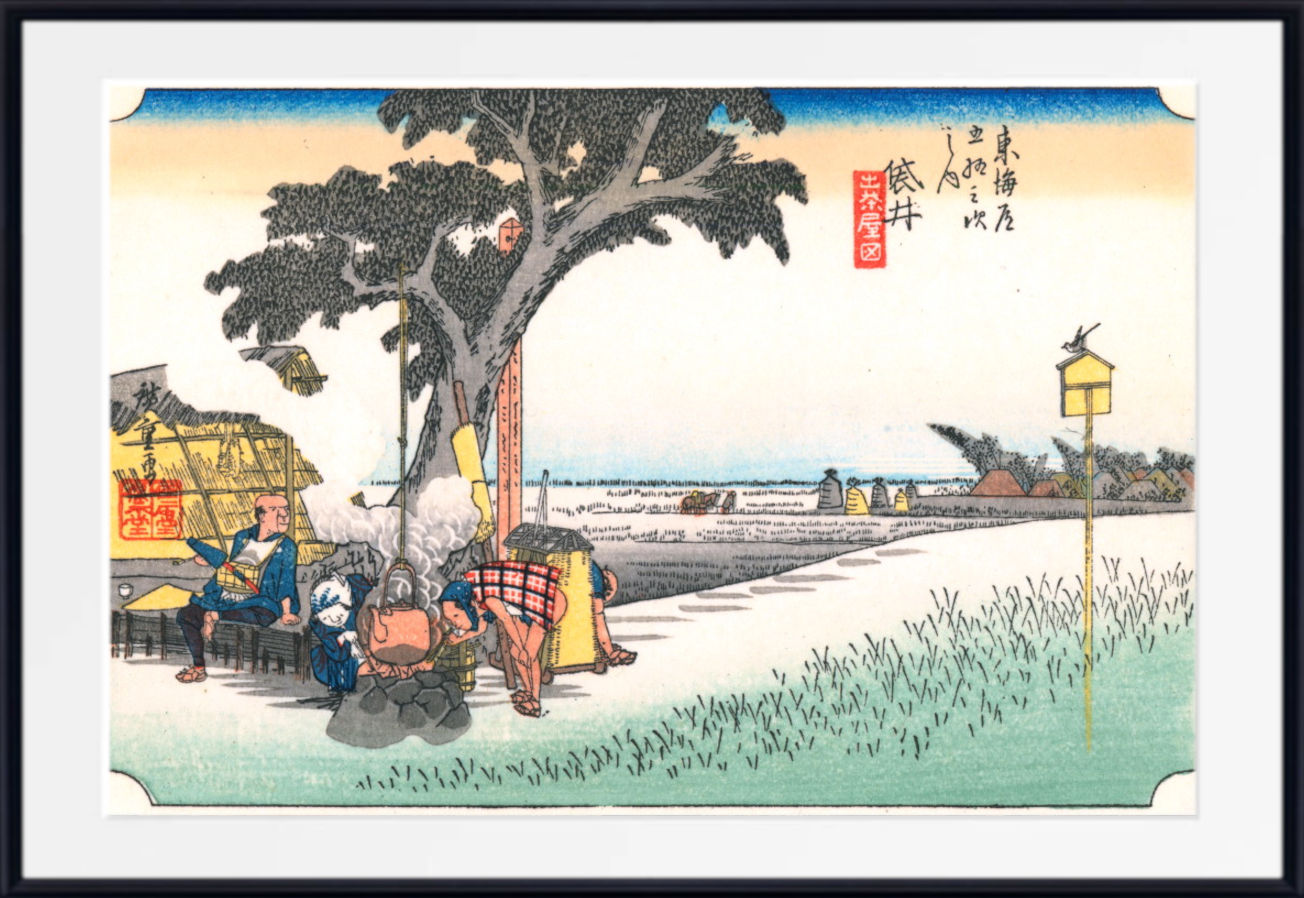 A framed Japanese ukiyo-e woodblock print showing a coastal scene with figures under a large tree near the shore, rendered in muted blue, beige, green, and black tones with a white mat and black frame.