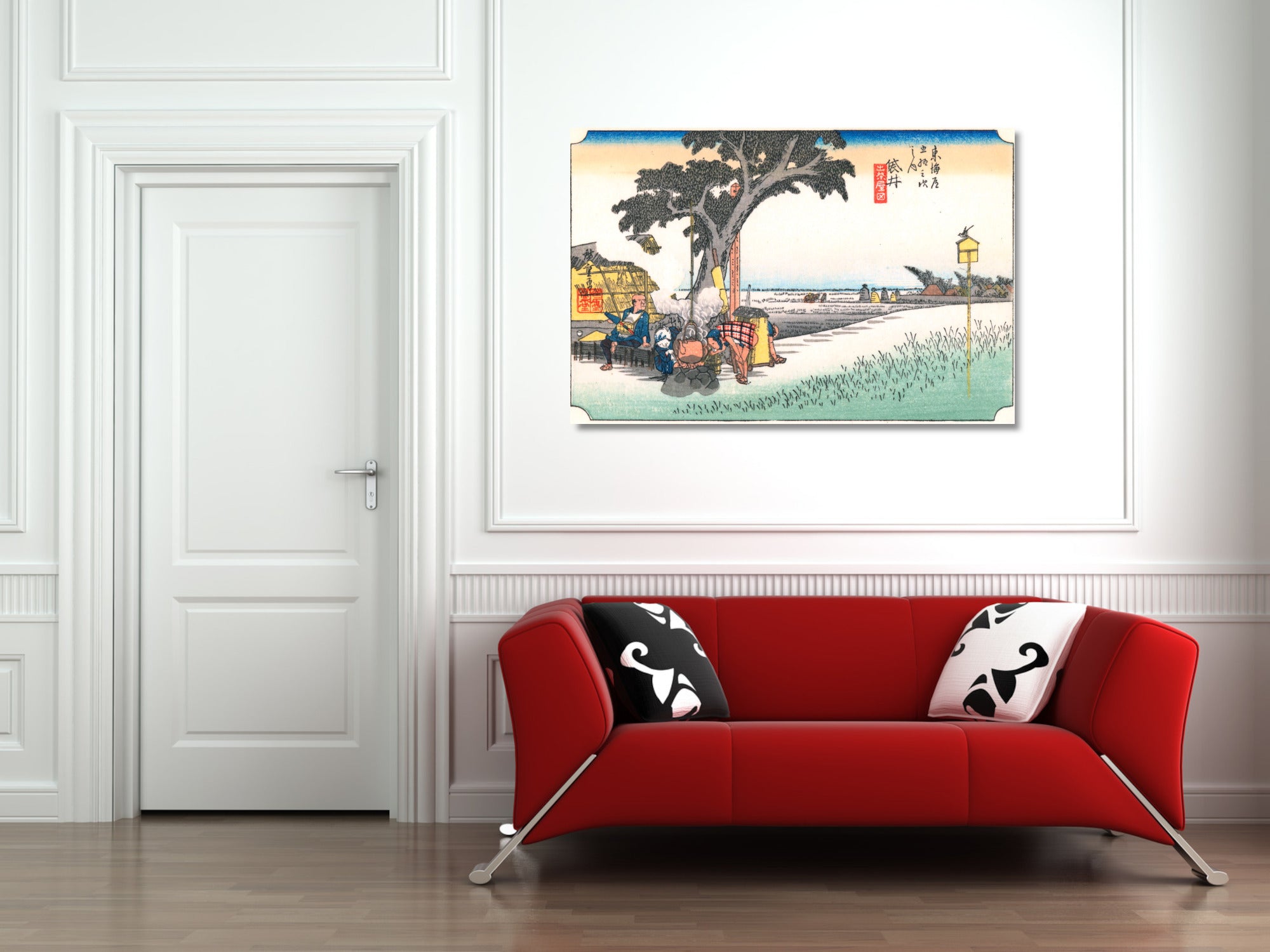 A framed Japanese-style landscape art print hangs on a white paneled wall above a modern red sofa with black and white patterned pillows in a bright room.