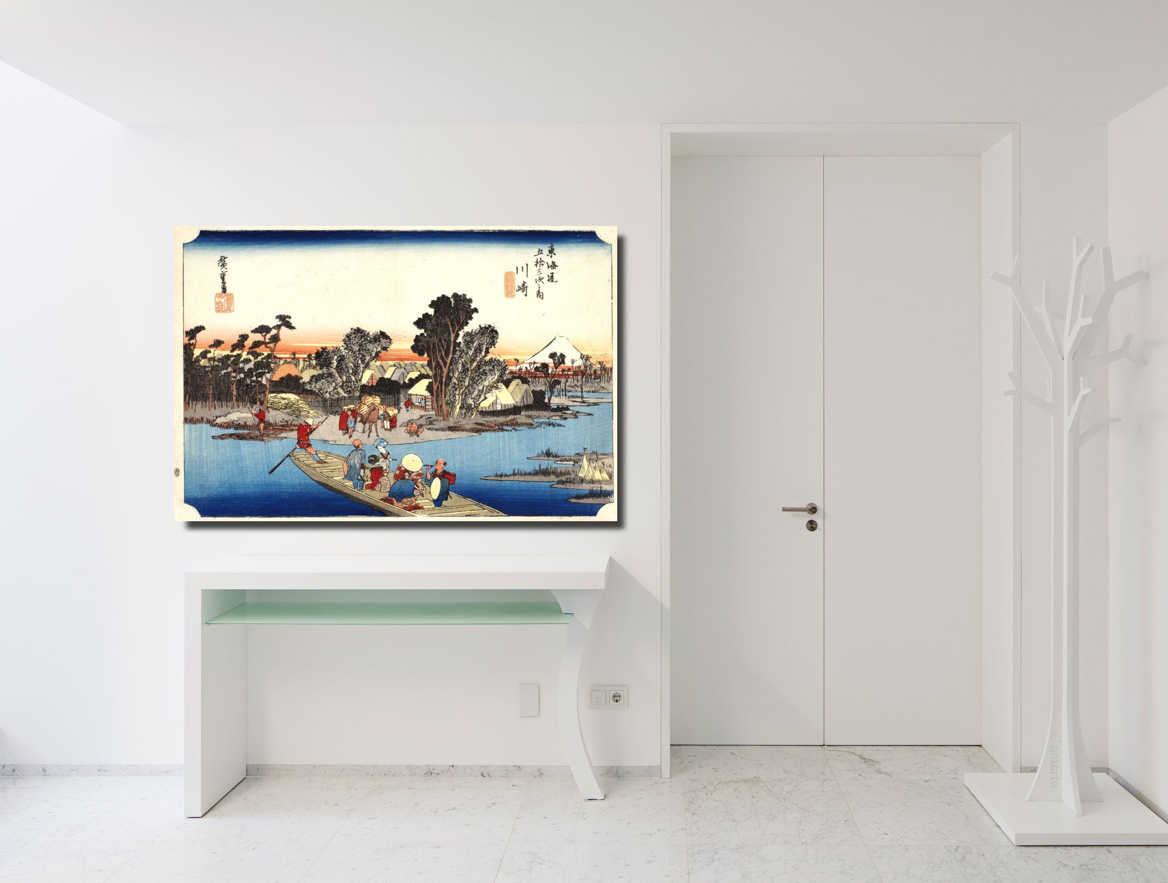 A framed Japanese ukiyo-e woodblock print depicting a boat scene by a river, displayed on a white wall above a console table in a bright, modern white room.