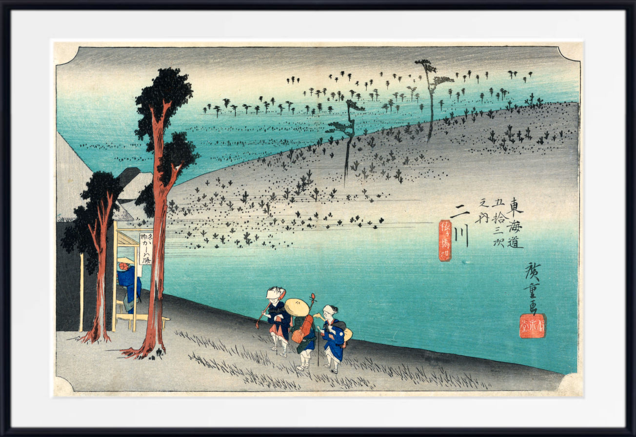 A framed Japanese-style art print depicting a coastal landscape with turquoise water, a sandy shoreline, several small figures near the bottom, and trees on the left. The print is shown with a wide white mat and a black frame against a plain white background.