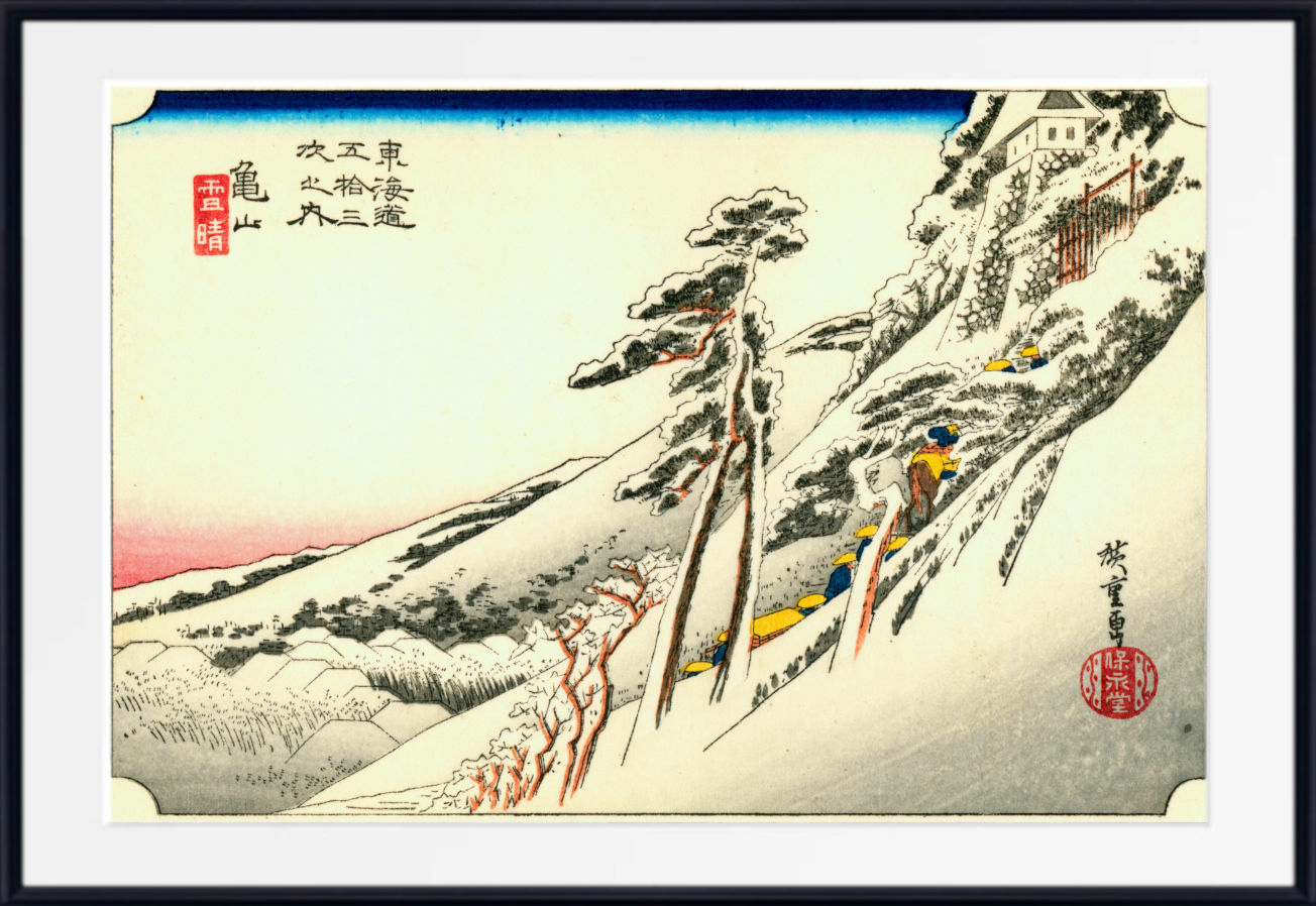A framed Japanese ukiyo-e woodblock print showing a snowy mountain scene with a lone figure climbing a steep path. The artwork includes black ink trees and rock details, a pale blue sky band at the top, a pink horizon glow, and red seals and accents.