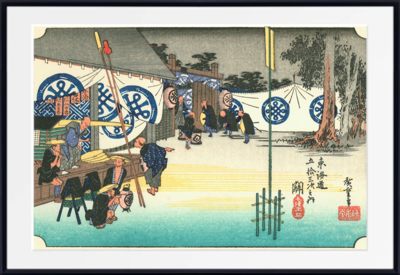 A framed Japanese ukiyo-e woodblock print showing a street scene with figures, boats, trees, and blue circular motifs, presented with a white mat and black frame.
