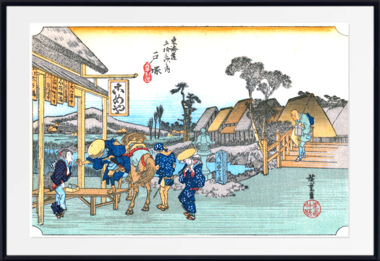 A framed Japanese ukiyo-e woodblock print depicting a village scene with figures, a horse, boats, and traditional buildings, shown against a white mat and black frame.
