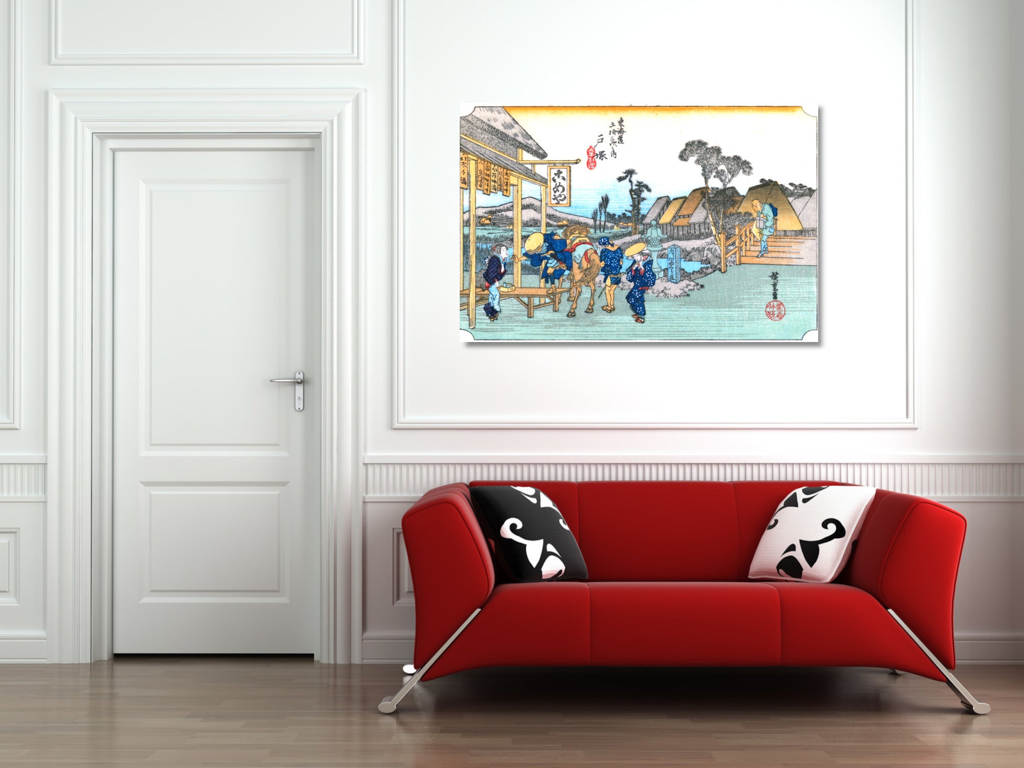 A framed Japanese ukiyo-e style art print depicting a street scene with figures and boats, displayed on a white wall above a modern red sofa with black and white patterned pillows.