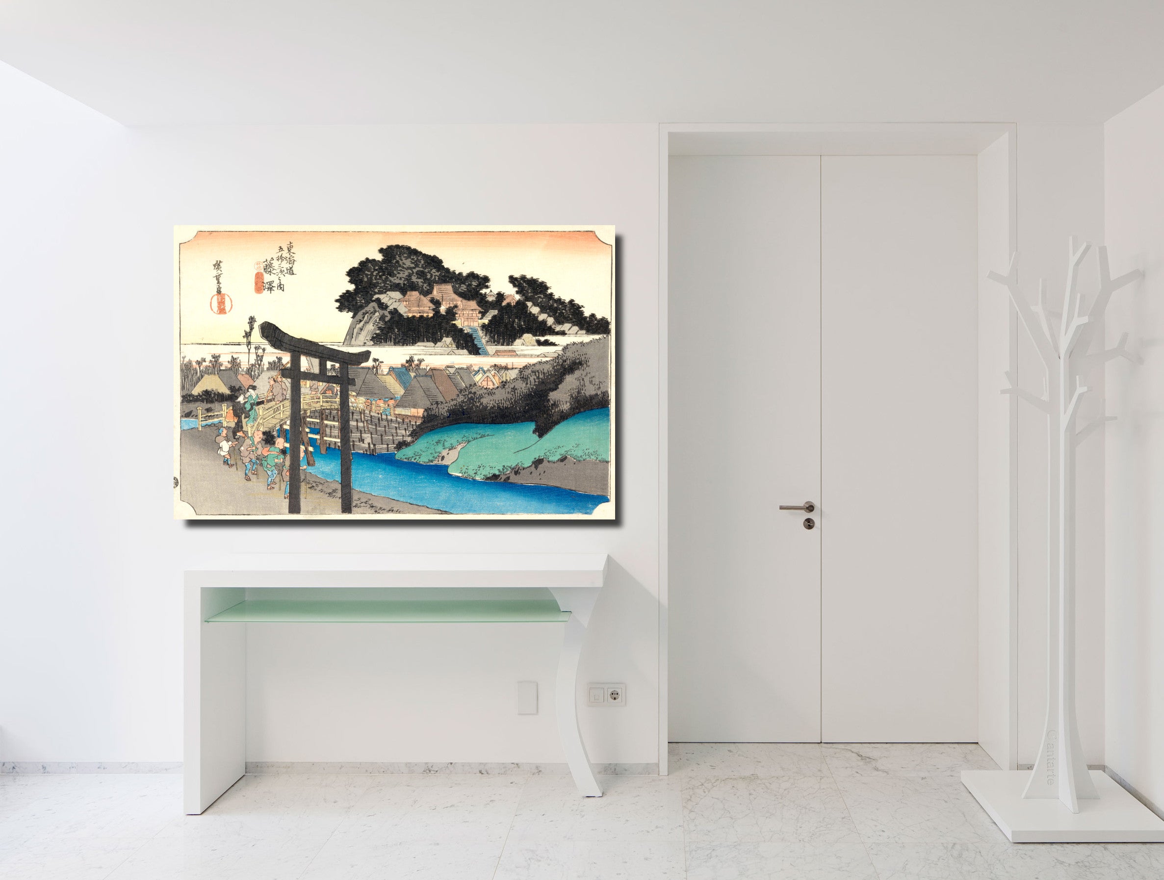 A framed art print of a Japanese ukiyo-e woodblock scene, depicting a torii gate, mountains, and blue water, displayed on a white wall above a white console table in a minimalist room.