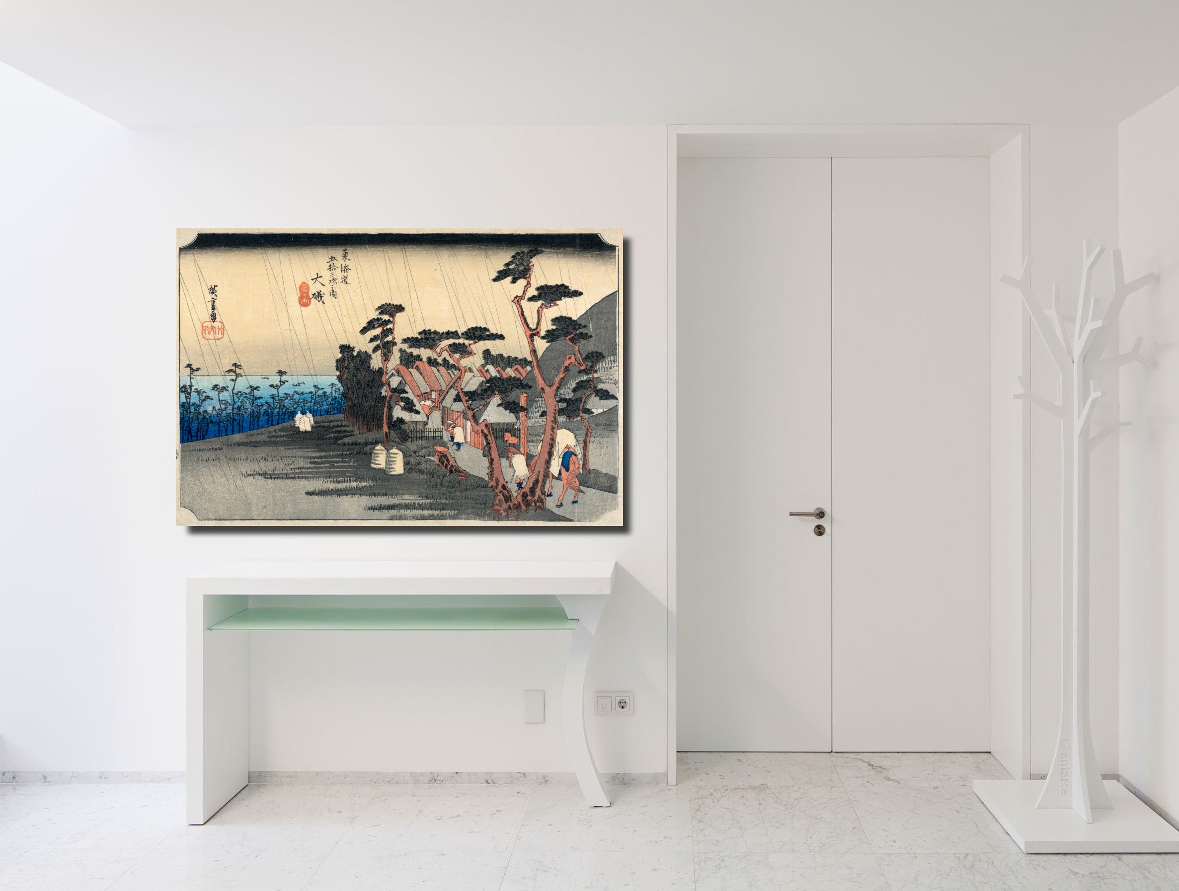 A framed Japanese ukiyo-e woodblock print depicting a rainy street scene with trees and figures, displayed on a white wall above a console table in a minimalist white interior.