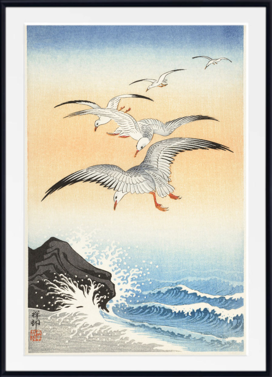 A framed Japanese-style art print depicting three white gulls flying over a blue ocean with white waves and a dark rocky shore under a pale sky.