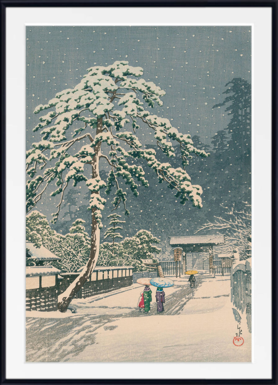 A framed Japanese-style snow landscape print showing a large snow-covered tree beside a path, with small figures under umbrellas and dark evergreen trees in the background. The artwork is presented with a white mat and black frame.