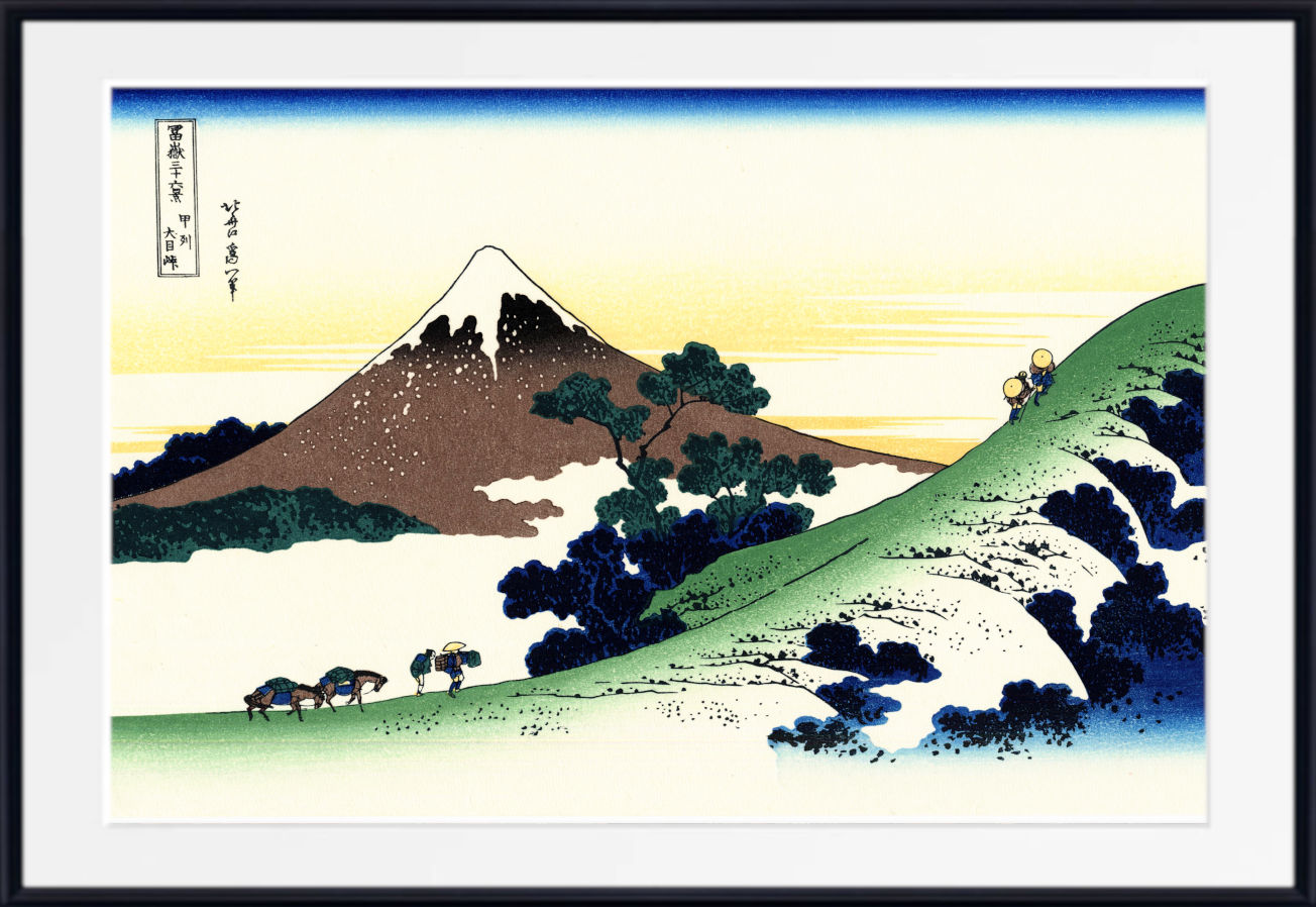 A framed Japanese-style landscape print showing a snow-capped mountain, green hills, trees, and small figures, presented with a white mat and black frame.