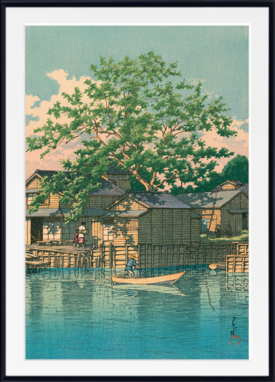 A framed Japanese-style art print depicting a serene lakeside village scene with wooden houses, a large green tree, and a small boat on blue water under a pale sky.