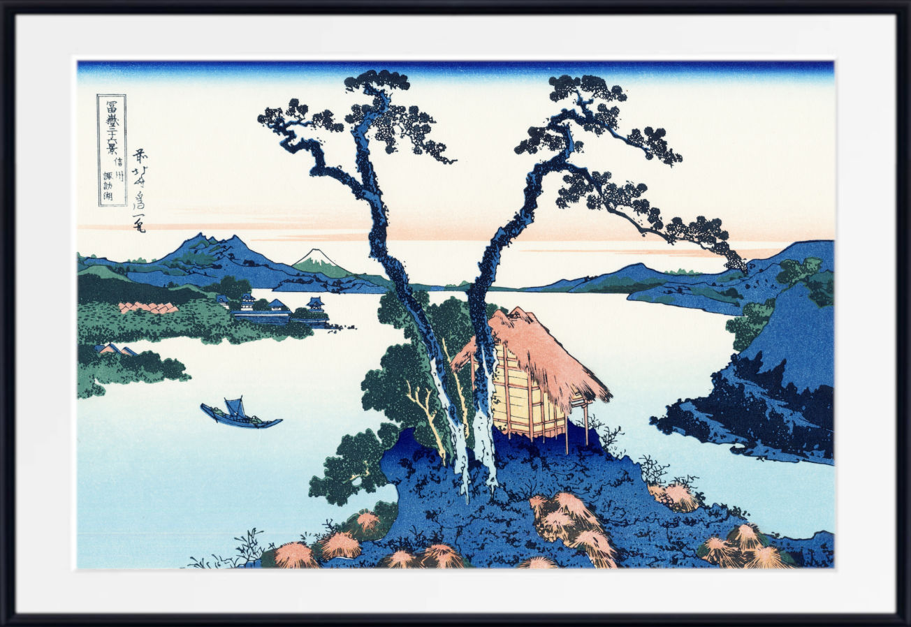 A framed Japanese-style landscape print showing a small thatched-roof cottage beside a calm lake, with mountains in the background, blue trees, and a boat on the water. The artwork is presented with a white mat and black frame.