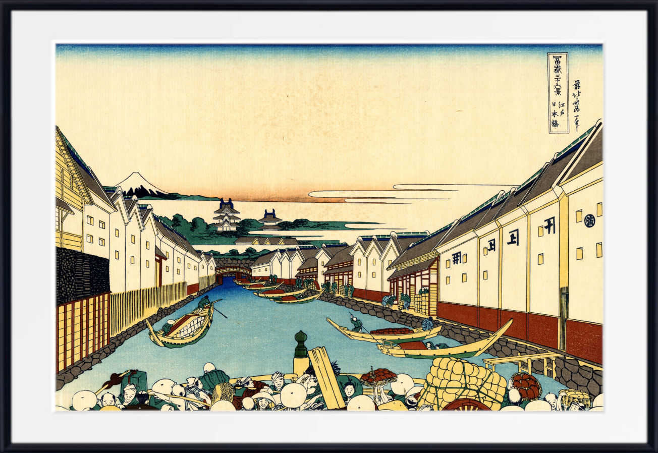 A framed Japanese ukiyo-e woodblock print depicting a canal scene with boats, buildings, mountains, and a pale sky, shown with a white mat and black frame.