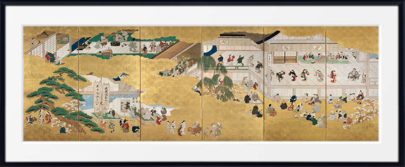 A framed Japanese-style artwork showing a detailed scene with many small figures, buildings, trees, and landscape elements on a gold-toned background, presented with a white mat and black frame.