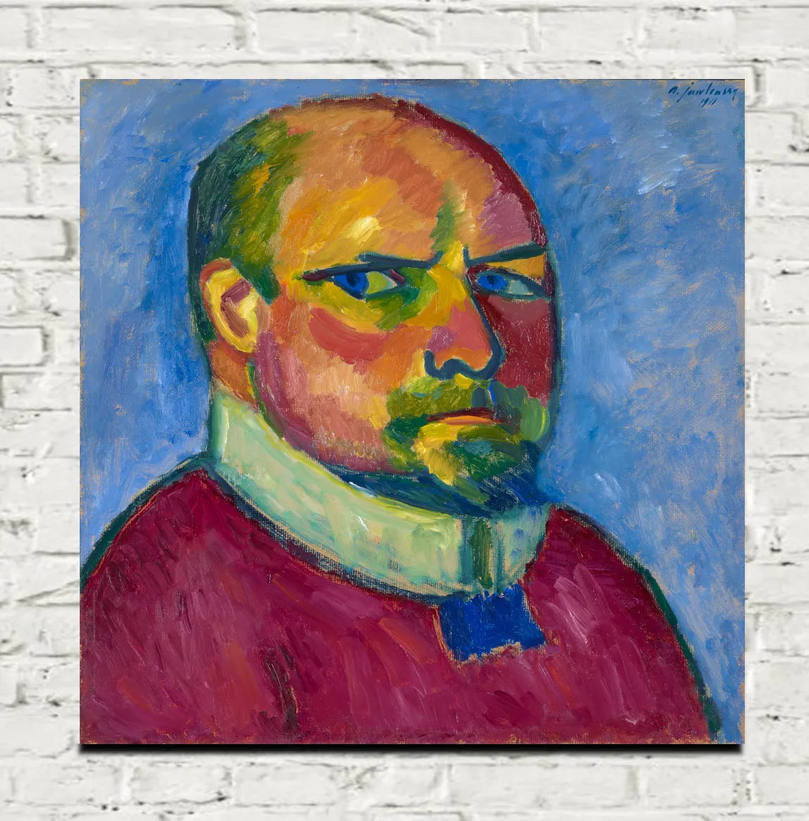 A colorful portrait painting of a man with a bald head, blue eyes, and a green beard, wearing a red shirt and white collar, displayed on a white brick wall. Alexej von Jawlensky, Self Portrait (1911)