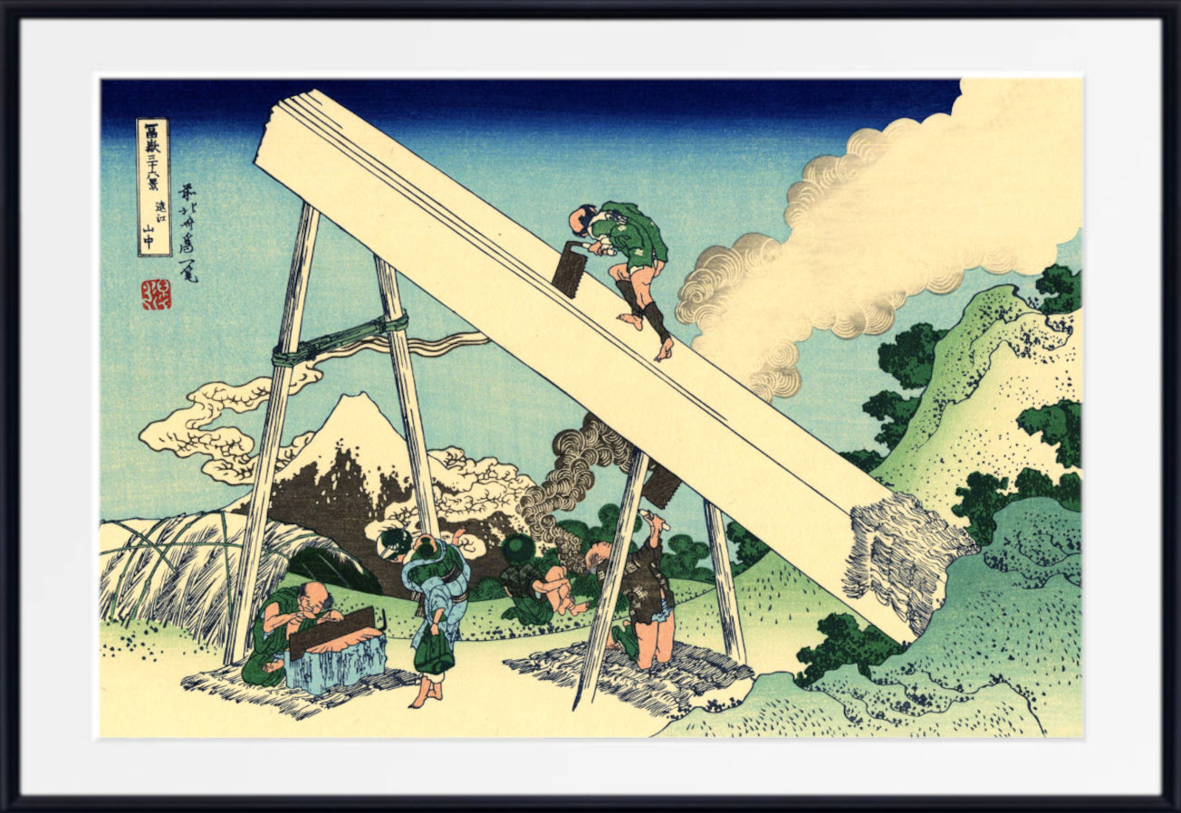 A framed Japanese ukiyo-e woodblock print showing workers moving a massive wooden beam with a pulley system, set against a landscape with mountains and clouds.