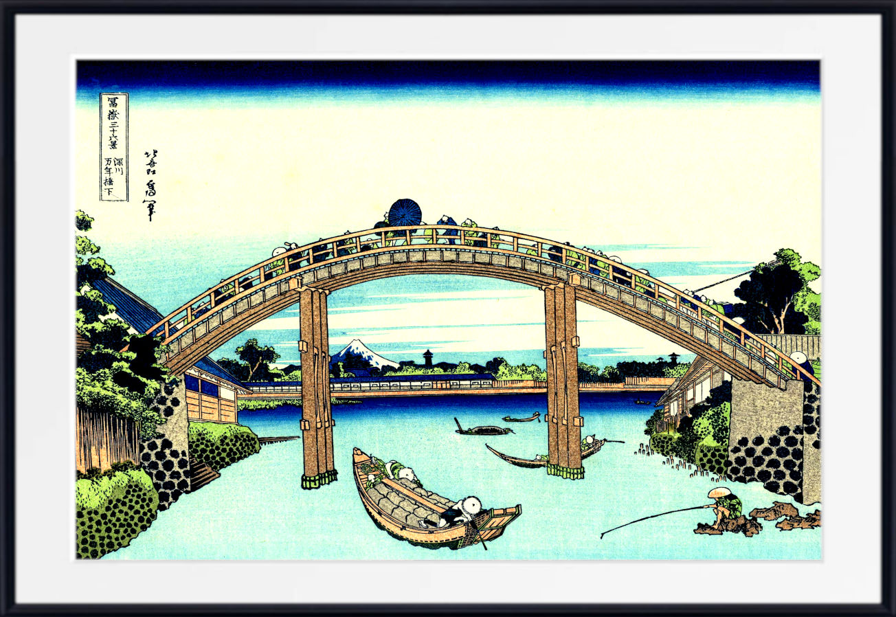 A framed Japanese-style art print depicting an arched wooden bridge over a calm blue river, with small boats, trees, and buildings. The print is shown with a wide white mat and a black frame.