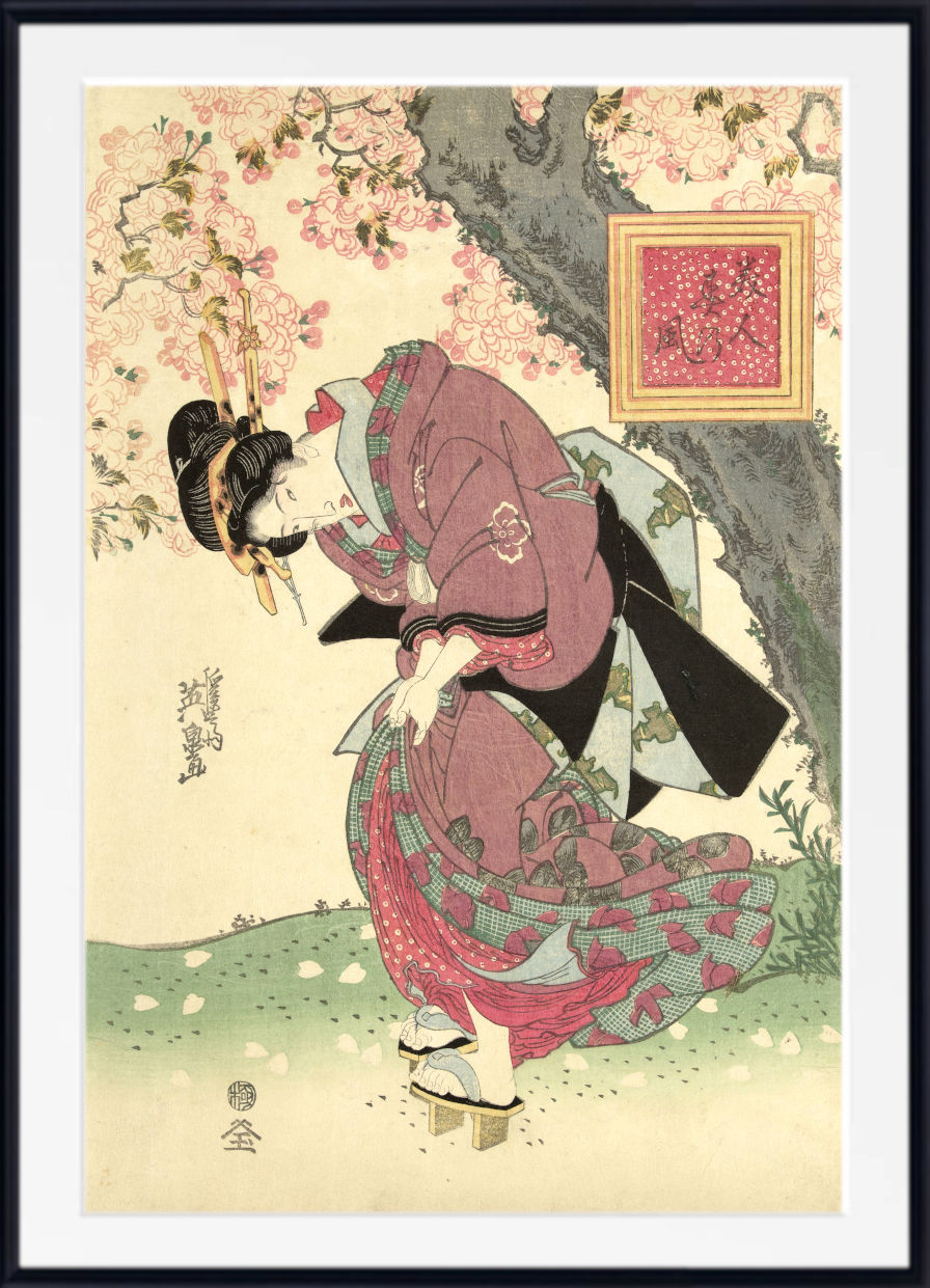 A framed Japanese ukiyo-e woodblock print featuring a woman in a flowing pink and green kimono beneath blooming cherry blossom trees, with a small framed artwork hanging on the wall. The print is shown with a white mat and black frame.