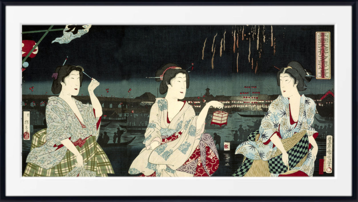 A framed Japanese ukiyo-e woodblock print depicting three women in traditional patterned kimonos seated by a river at night, with fireworks visible in the sky above. The print is shown within a white mat and a black frame.