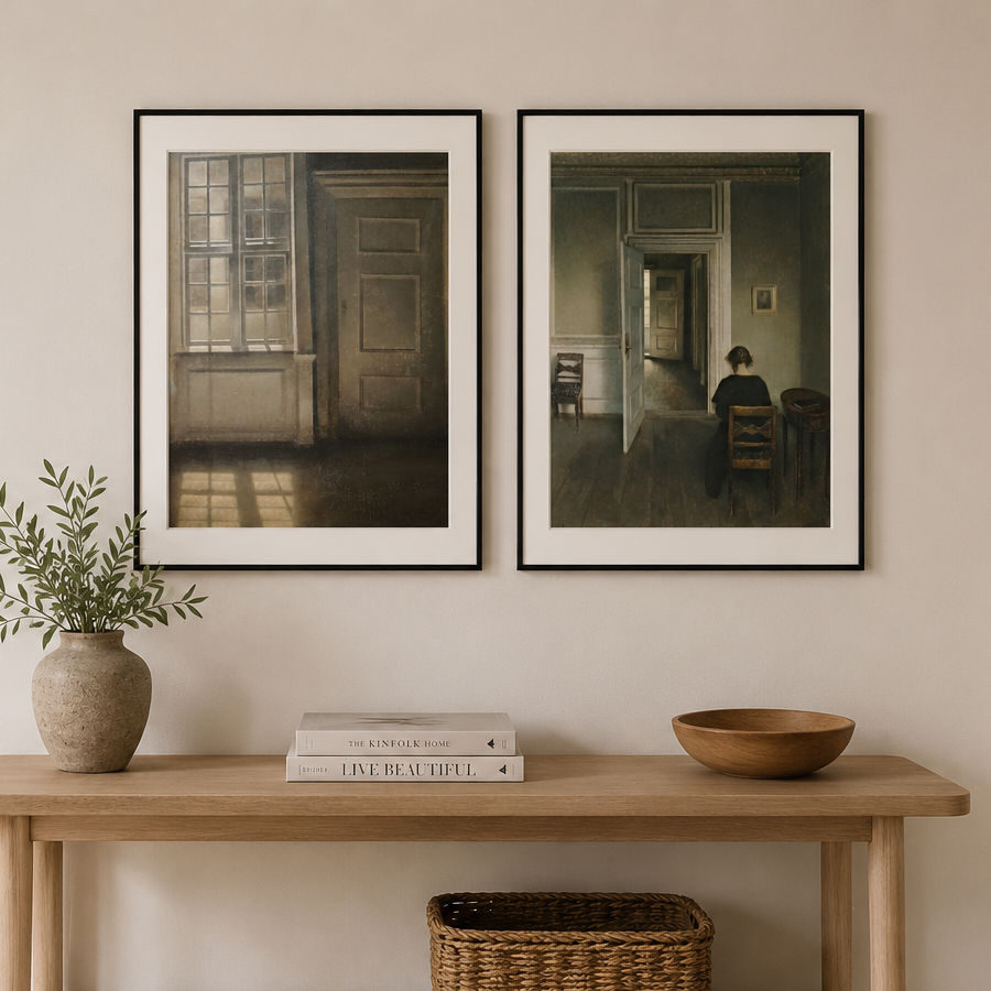 Two framed Hammershoi prints with black frames and white mats hang on a beige wall above a wooden console table styled with a plant, books, a bowl, and a basket.