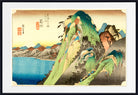 A framed Japanese-style landscape print showing a steep green and blue mountain beside a blue body of water, with a cream sky and red seal markings, presented in a black frame with white matting.