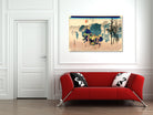 A framed Japanese ukiyo-e woodblock print depicting a samurai warrior scene, displayed on a white wall above a modern red sofa with black and white patterned pillows.