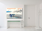 A framed Japanese ukiyo-e style art print depicting Mount Fuji and figures in a snowy landscape, displayed on a white console table in a bright, modern white room.