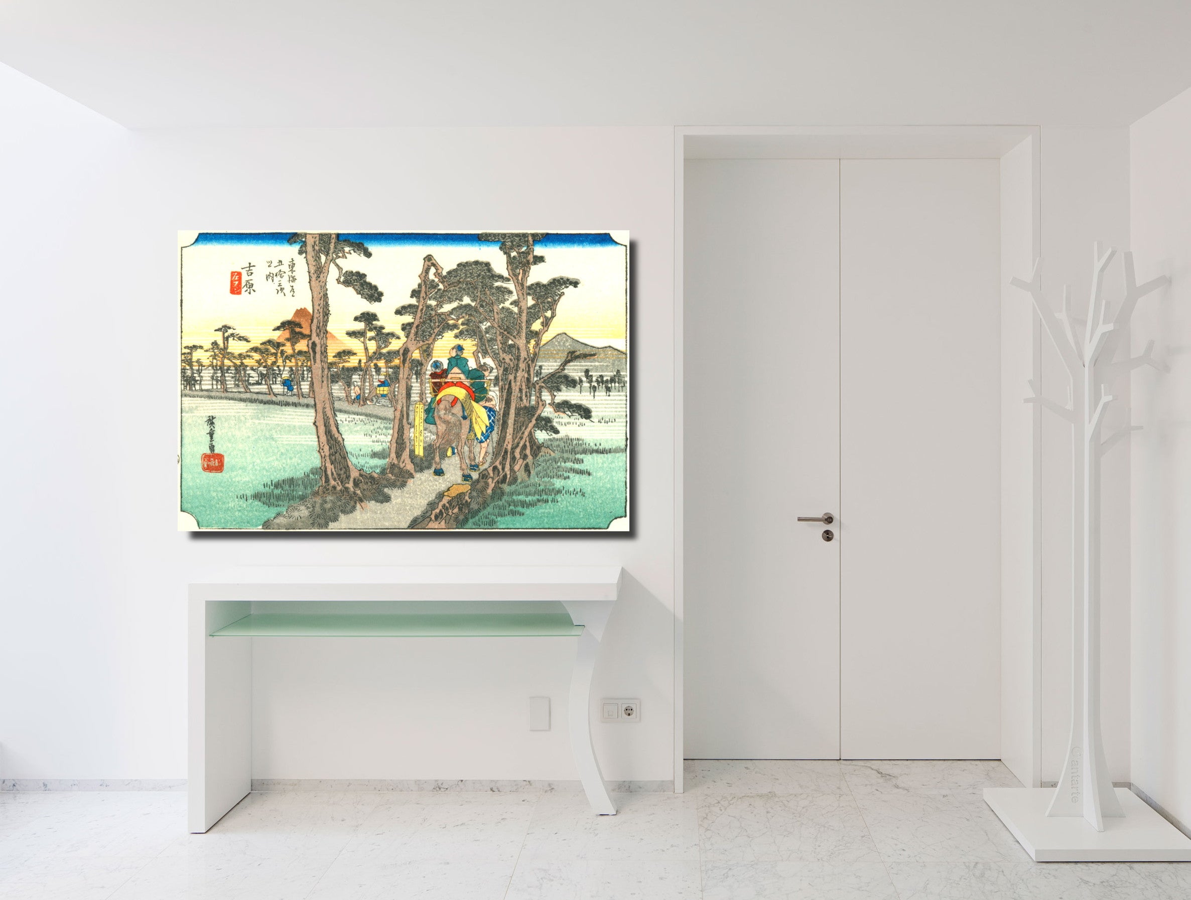 A framed Japanese ukiyo-e woodblock print depicting a scenic landscape with figures, mounted on a white wall above a white console table in a minimalist, modern room.