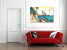 A framed Japanese-style landscape art print hangs on a white paneled wall above a red sofa with black and white patterned pillows in a modern living room setting.