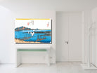 A framed Japanese ukiyo-e style art print depicting a harbor scene with blue water, boats, and mountains, displayed on a white console table in a minimalist white room.