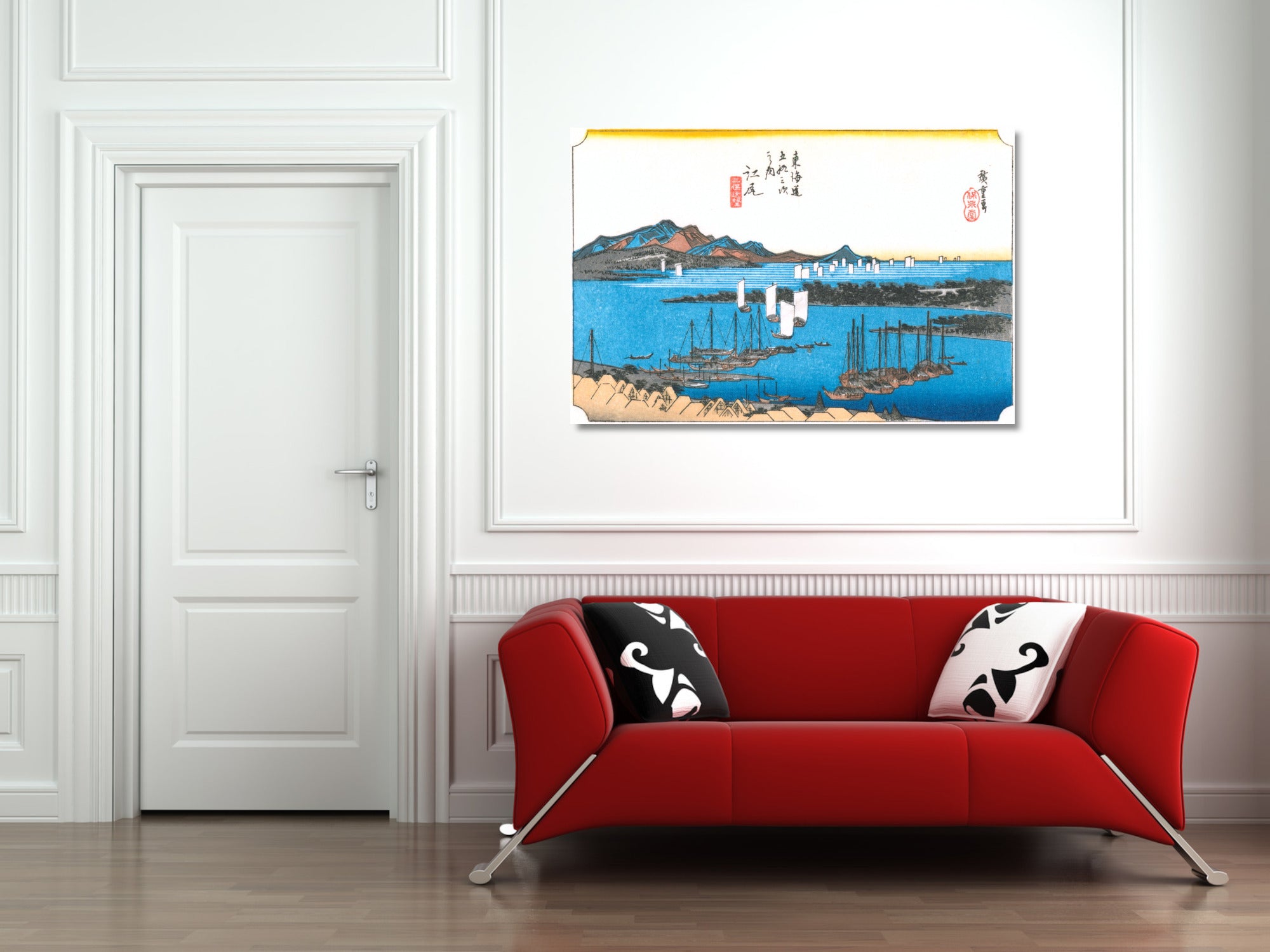 A framed Japanese-style landscape art print with blue water, mountains, and boats hangs on a white paneled wall above a red sofa with black-and-white pillows.
