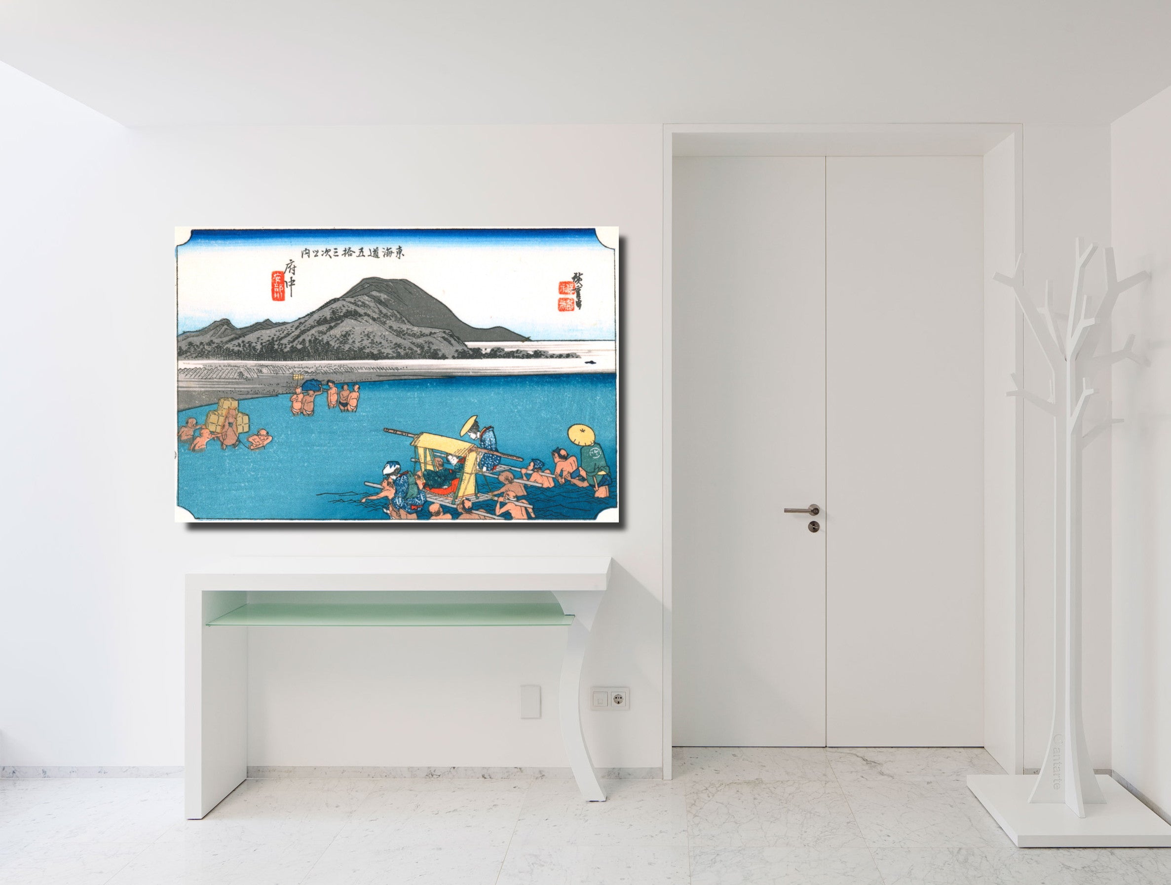 A framed art print depicting a traditional Japanese coastal scene with a mountain and fishermen, displayed on a white console table in a minimalist, modern white room.