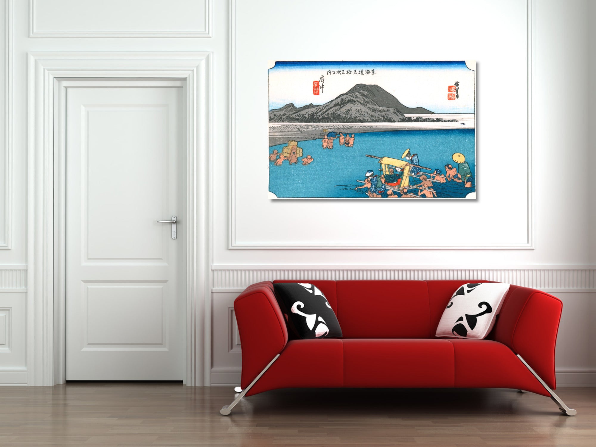 A framed art print depicting a traditional Japanese landscape with a mountain, blue water, and small boats, displayed on a white wall above a red sofa in a modern living room setting.