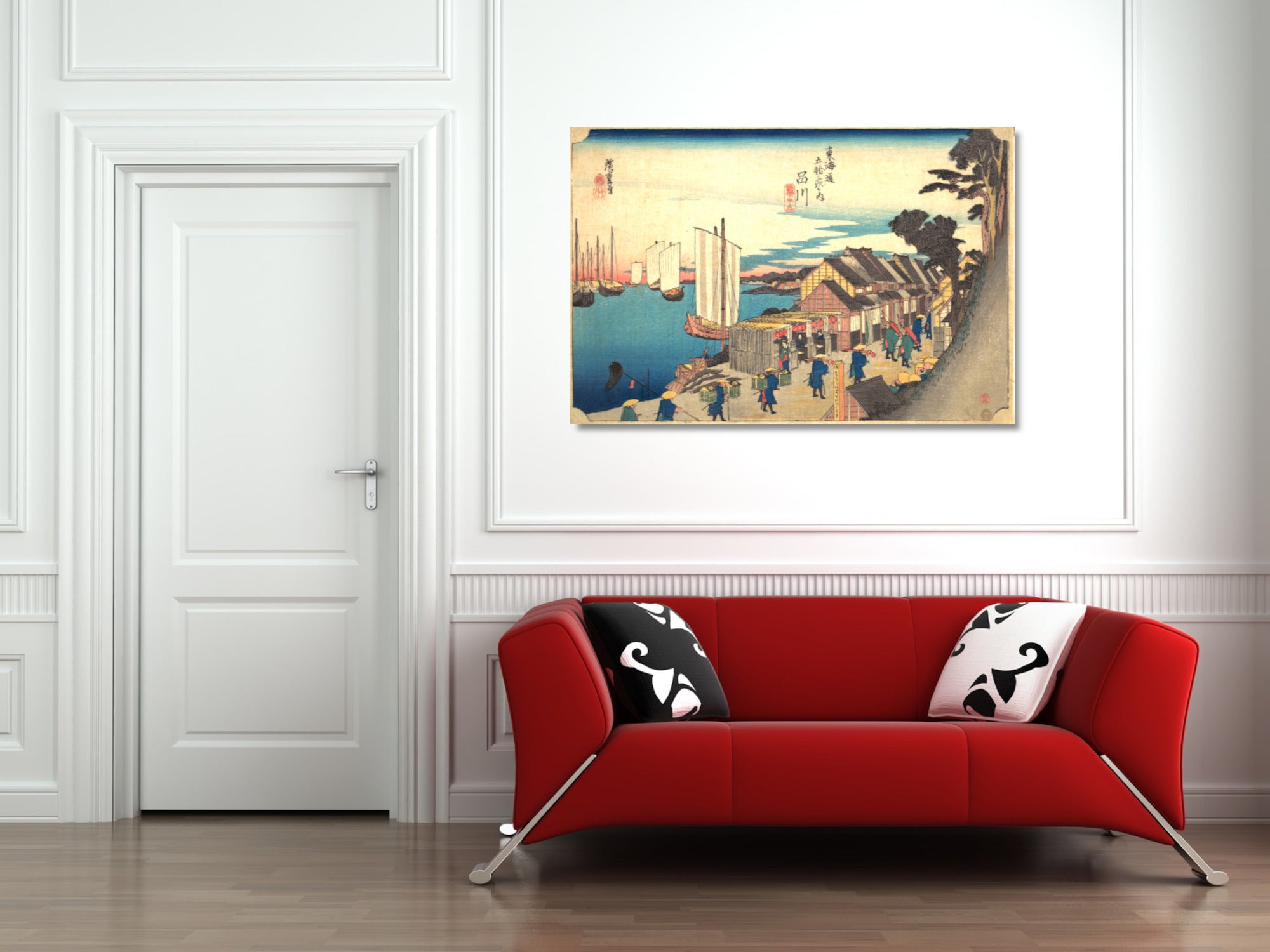 A framed Japanese-style art print depicting a harbor scene with boats and figures, displayed on a white wall above a modern red sofa with black-and-white patterned pillows.