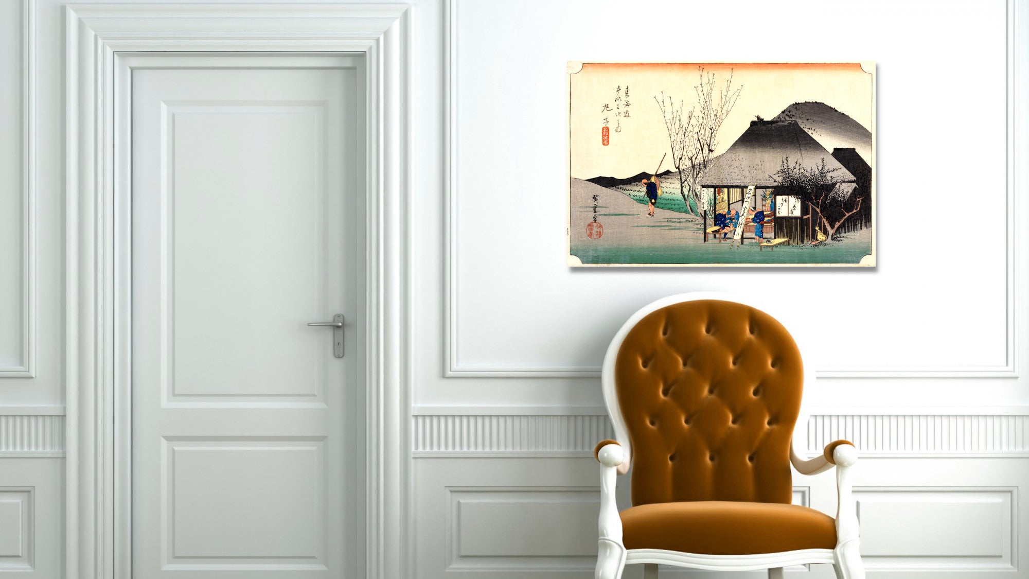 A framed Japanese-style art print depicting a traditional house and mountain scene, displayed on a white paneled wall above an orange tufted armchair.