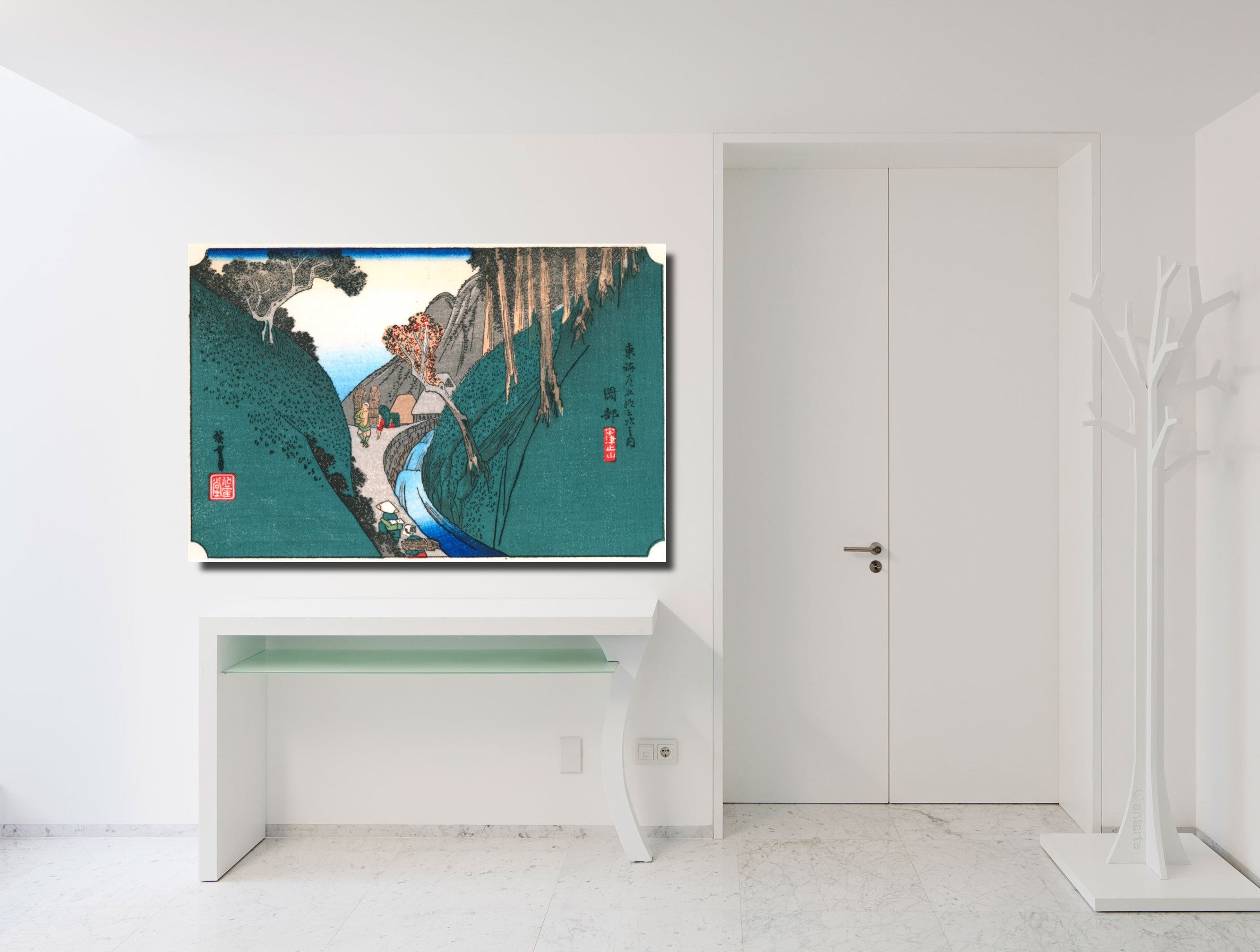 A framed Japanese ukiyo-e style art print depicting a mountain landscape with a river and figures, displayed on a white wall above a console table in a bright, modern white room.