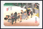 A framed Japanese-style art print depicting a street scene with people, horses, crates, and buildings, shown against a white background with a black frame border.