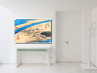 A framed Japanese ukiyo-e woodblock print depicting a river landscape with figures and boats, displayed on a white wall above a white console table in a minimalist room.