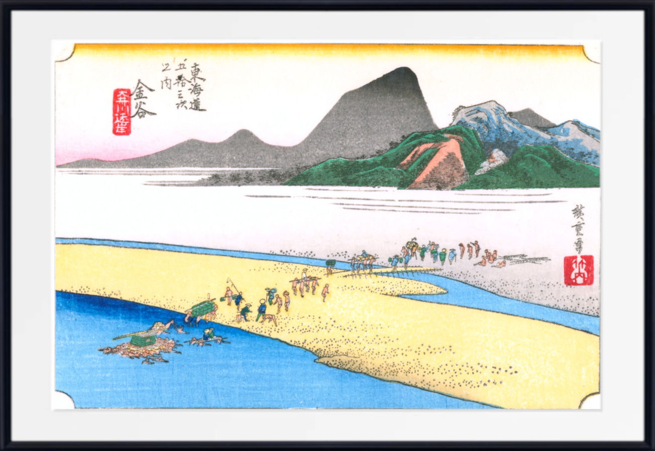 A framed Japanese-style art print depicting a coastal landscape with mountains, blue water, pale sand, and small figures along the shore. The print is shown with a white mat and black frame against a light neutral background.