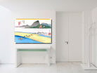 A framed Japanese ukiyo-e style landscape art print is displayed on a white wall above a white console table in a bright, modern room. The print features a scenic river landscape with mountains, boats, and figures, rendered in traditional colors of blue, yellow, green, and red.