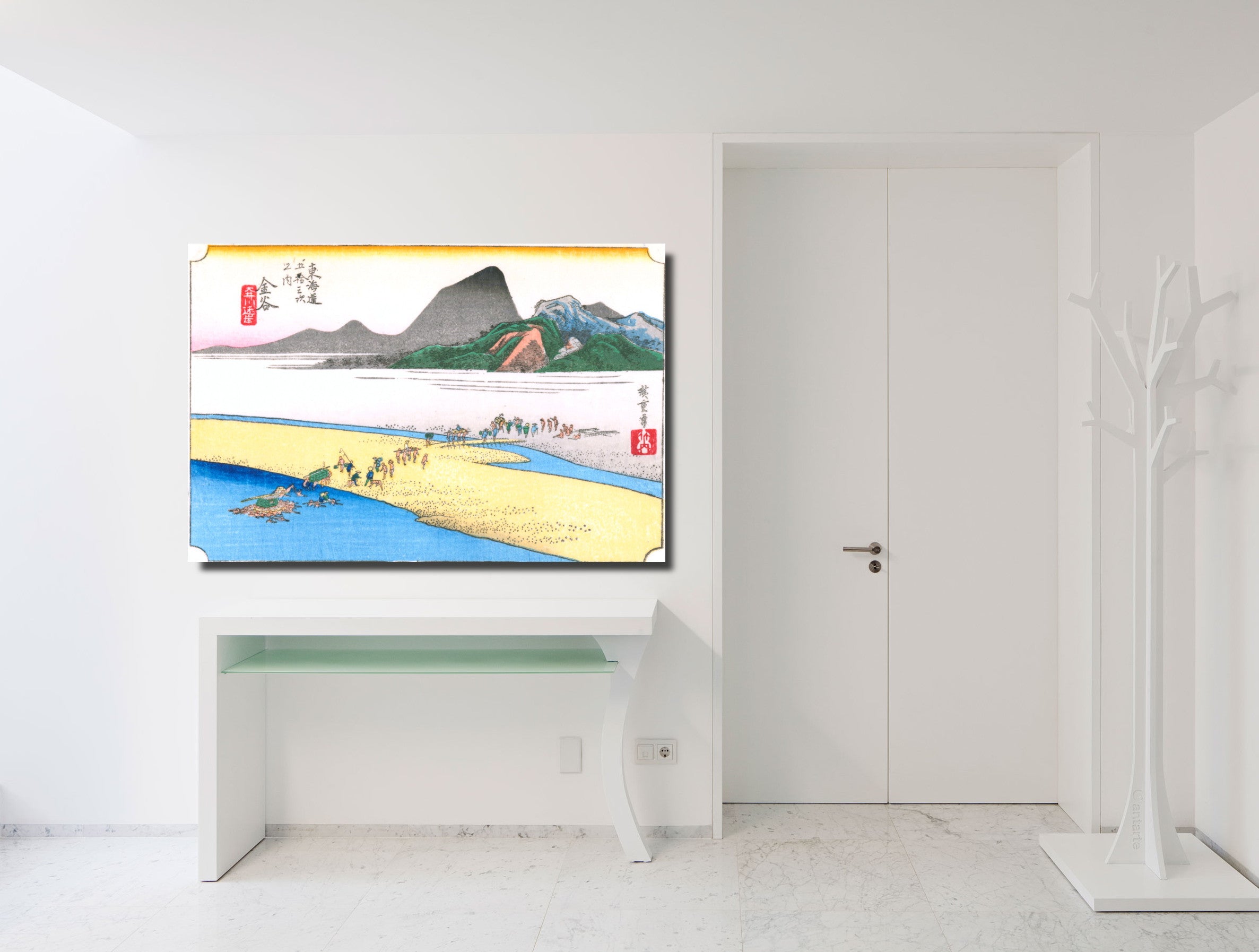 A framed Japanese ukiyo-e style landscape art print is displayed on a white wall above a white console table in a bright, modern room. The print features a scenic river landscape with mountains, boats, and figures, rendered in traditional colors of blue, yellow, green, and red.