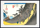 A framed Japanese-style art print depicting a mountain path with small figures walking along a yellow road, trees, blue water, and red seal marks, shown against a white mat and black frame.